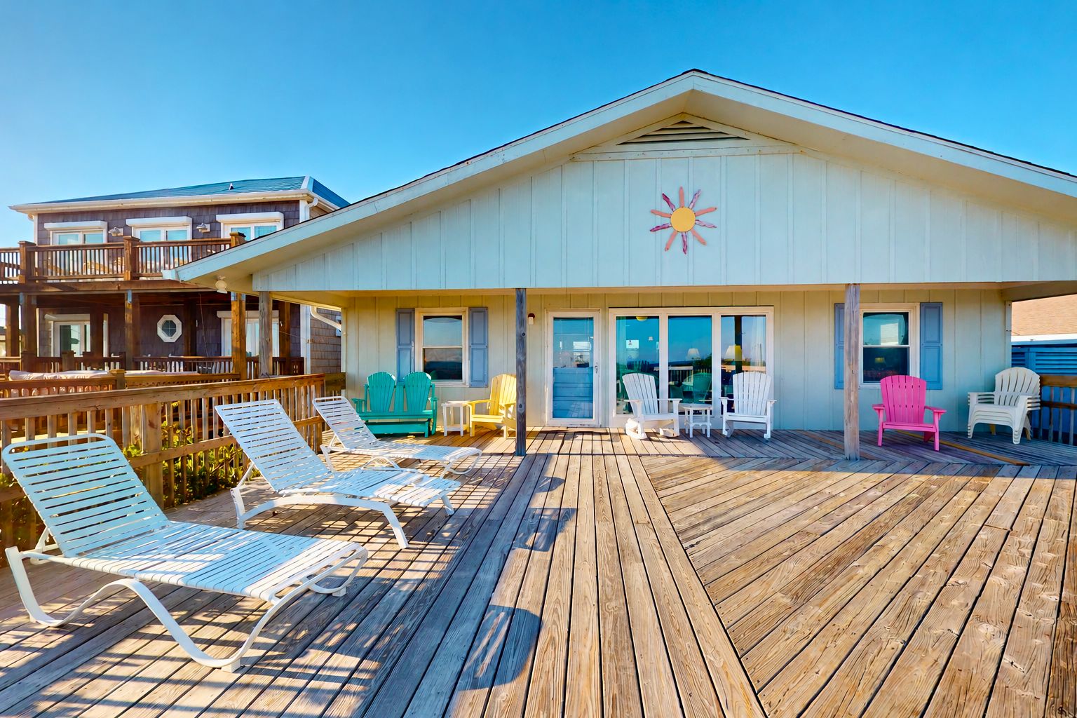 Una propiedad frente al mar con una terraza de madera, varios sillones Adirondack y un gran ventanal con vista al océano.