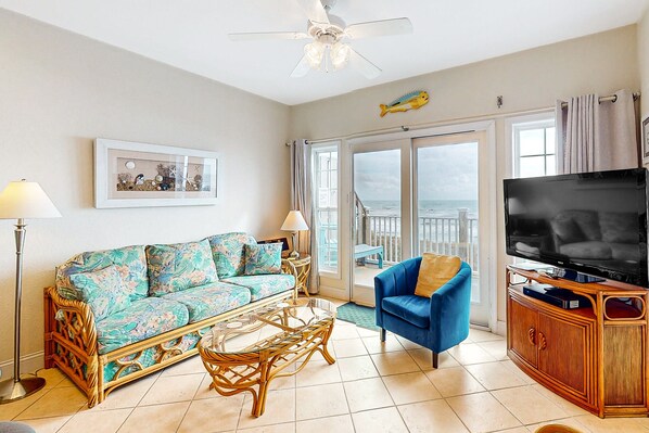 Un salon comprenant un canapé, un fauteuil, une télévision et un balcon avec vue sur la mer.