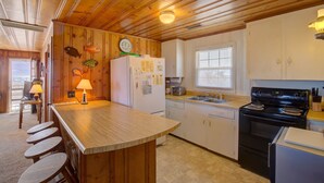 A kitchen with wooden cabinets, a refrigerator, a stove, and a bar area with stools. - 3BR Oceanfront Topsail Beach Cottage | Dog Friendly! (Topsail Beach)
