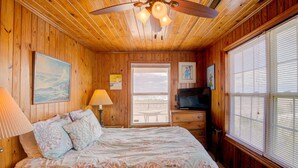 A wooden-paneled bedroom with a bed, a ceiling fan, a TV, and a window with blinds. - 3BR Oceanfront Topsail Beach Cottage | Dog Friendly! (Topsail Beach)