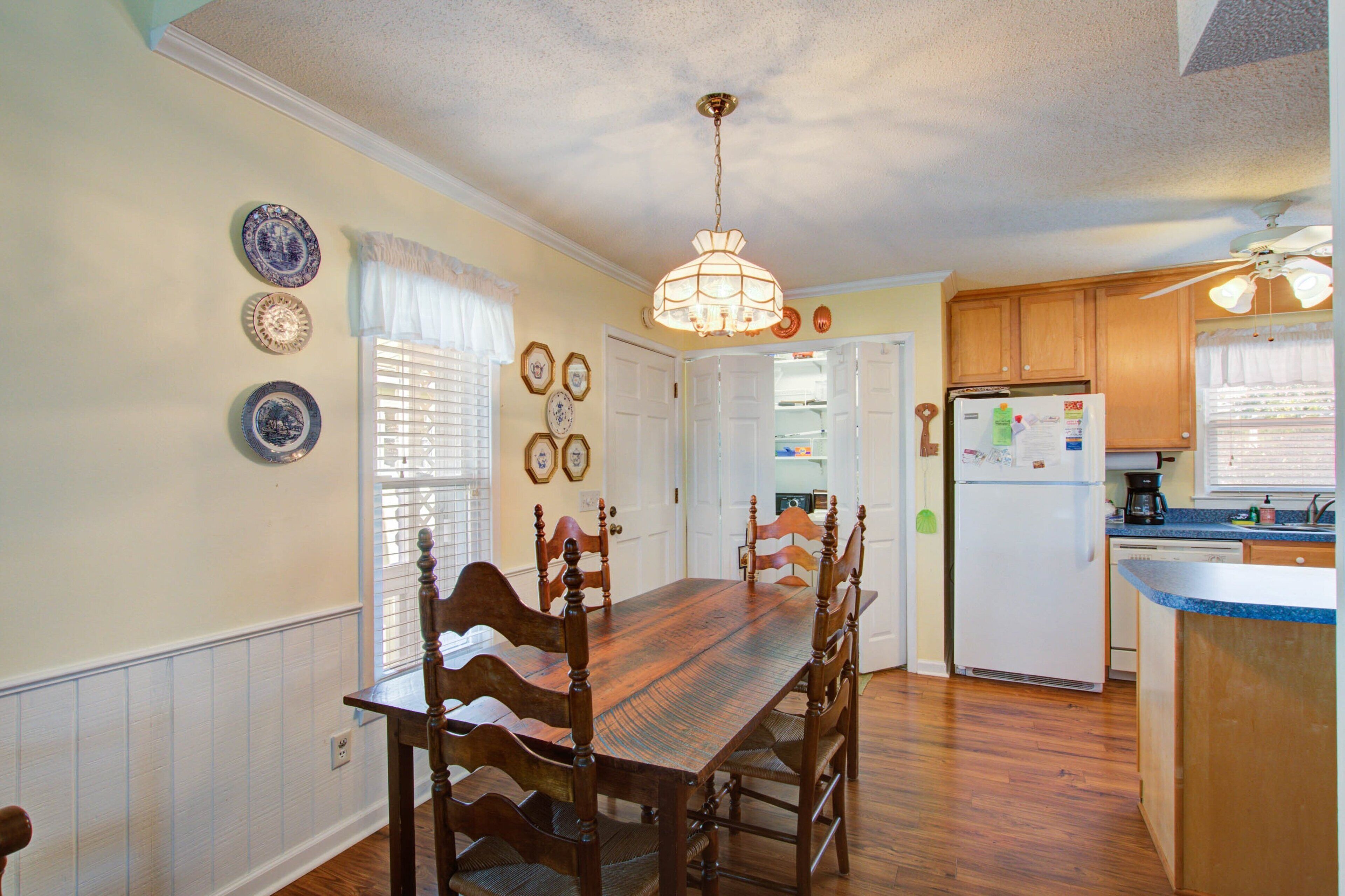 A dining area with a wooden table and chairs, a ceiling fan, and a refrigerator in the kitchen area.