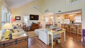Amplia sala de estar con sofá, una mesa de comedor y zona de cocina con armarios de madera y refrigerador.