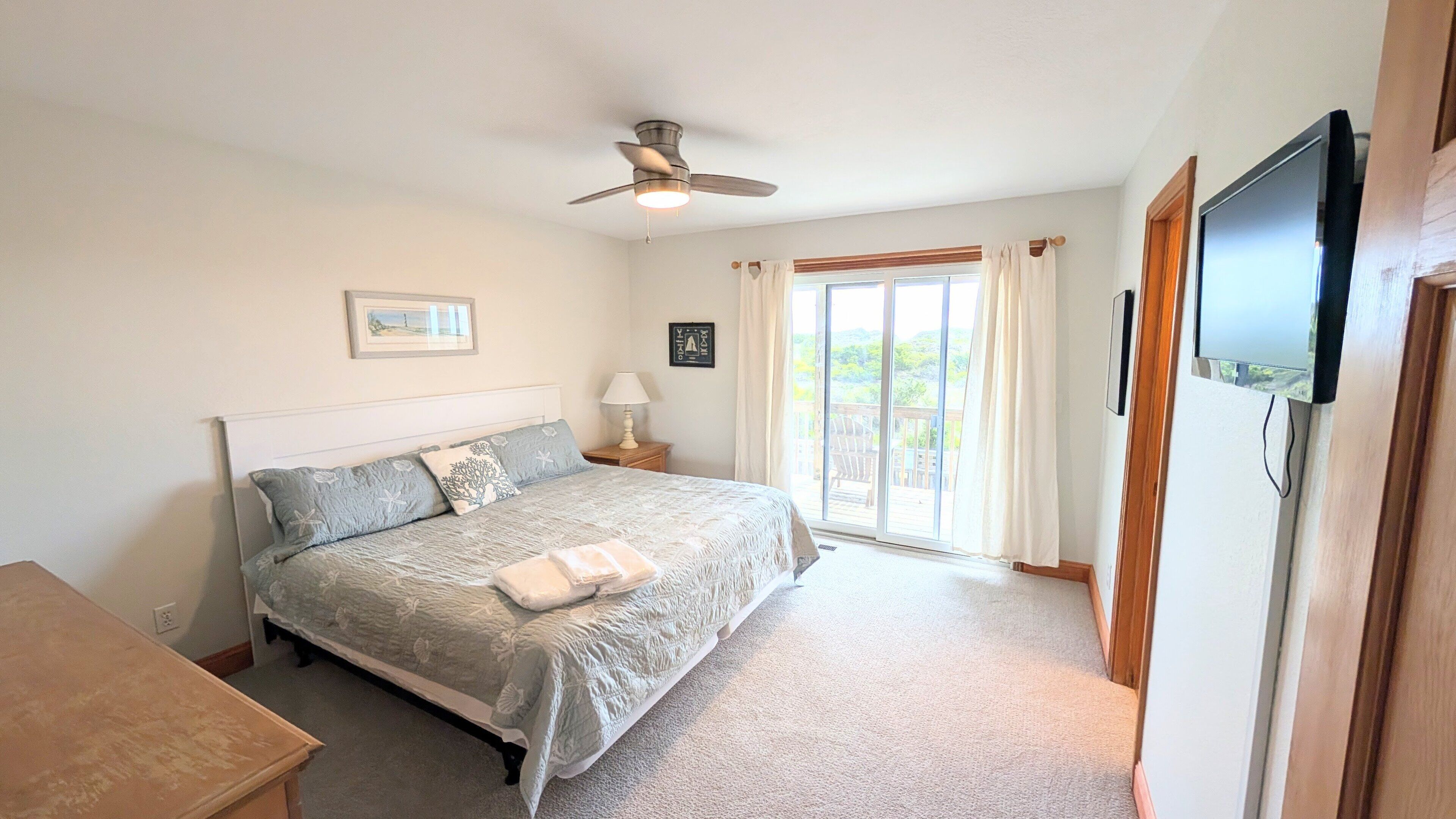 A bedroom with a bed, a ceiling fan, a nightstand, a lamp, a TV, and a sliding glass door leading to an outdoor area.