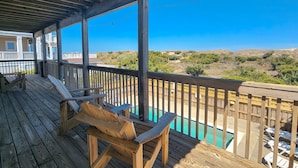 Eine Holzterrasse mit Pool, Holzstühlen und Blick auf eine hügelige Landschaft.