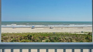Blick auf den Strand vom Balkon mit Holzgeländer, feinem Sand und dem Meer.
