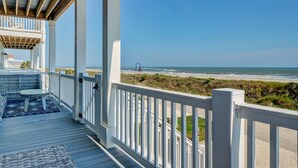 Eine überdachte Terrasse mit weißen Geländern, einem Tisch und Stühlen sowie Blick auf den Strand.