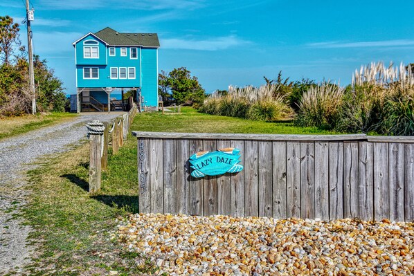 A blue house with a wooden fence and a sign that reads "Lazy Daze." - Dog-friendly, sound-front home with 2 sundecks, fireplace, & private hot tub (Buxton)