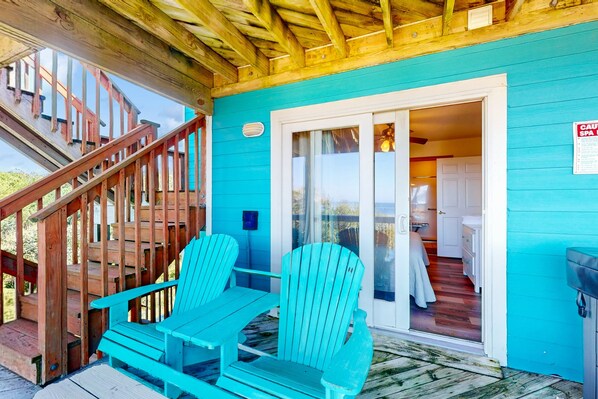 A turquoise cabin with a wooden staircase and two Adirondack chairs on the porch.