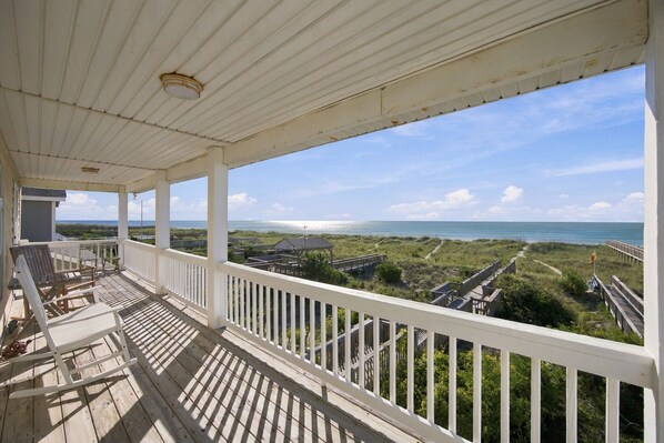 A covered porch with a view of the beach and a wooden structure in the distance.