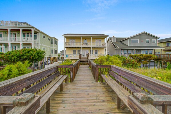 Une promenade en bois mène à une rangée de maisons situées en bord de mer, toutes dotées de balcons.