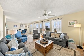 A spacious living room with a ceiling fan, a dining area with chairs, a sofa set, and a coffee table with decorative items.