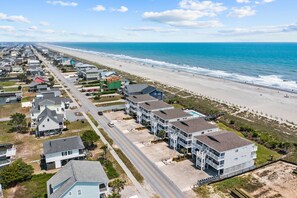 A coastal residential area with beachfront properties, including multi-story buildings with balconies and a road leading to the beach. - Lower Waterfront Condo with Oceanfront Balcony, Shared Outdoor Pool, WiFi & AC (Holden Beach)