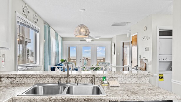 A modern kitchen with granite countertops, stainless steel appliances, and large windows offering views of the outdoors. - Lower Waterfront Condo with Oceanfront Balcony, Shared Outdoor Pool, WiFi & AC (Holden Beach)