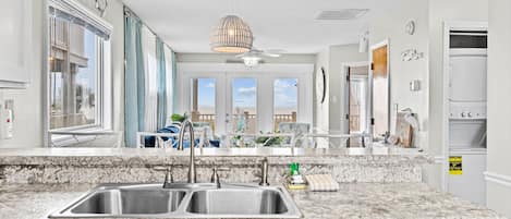 A modern kitchen with granite countertops, stainless steel appliances, and large windows offering views of the outdoors.