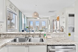 A modern kitchen with granite countertops, stainless steel appliances, and large windows offering views of the outdoors.