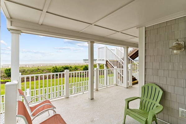 A covered porch with a view of the beach, white railings, and a green chair.