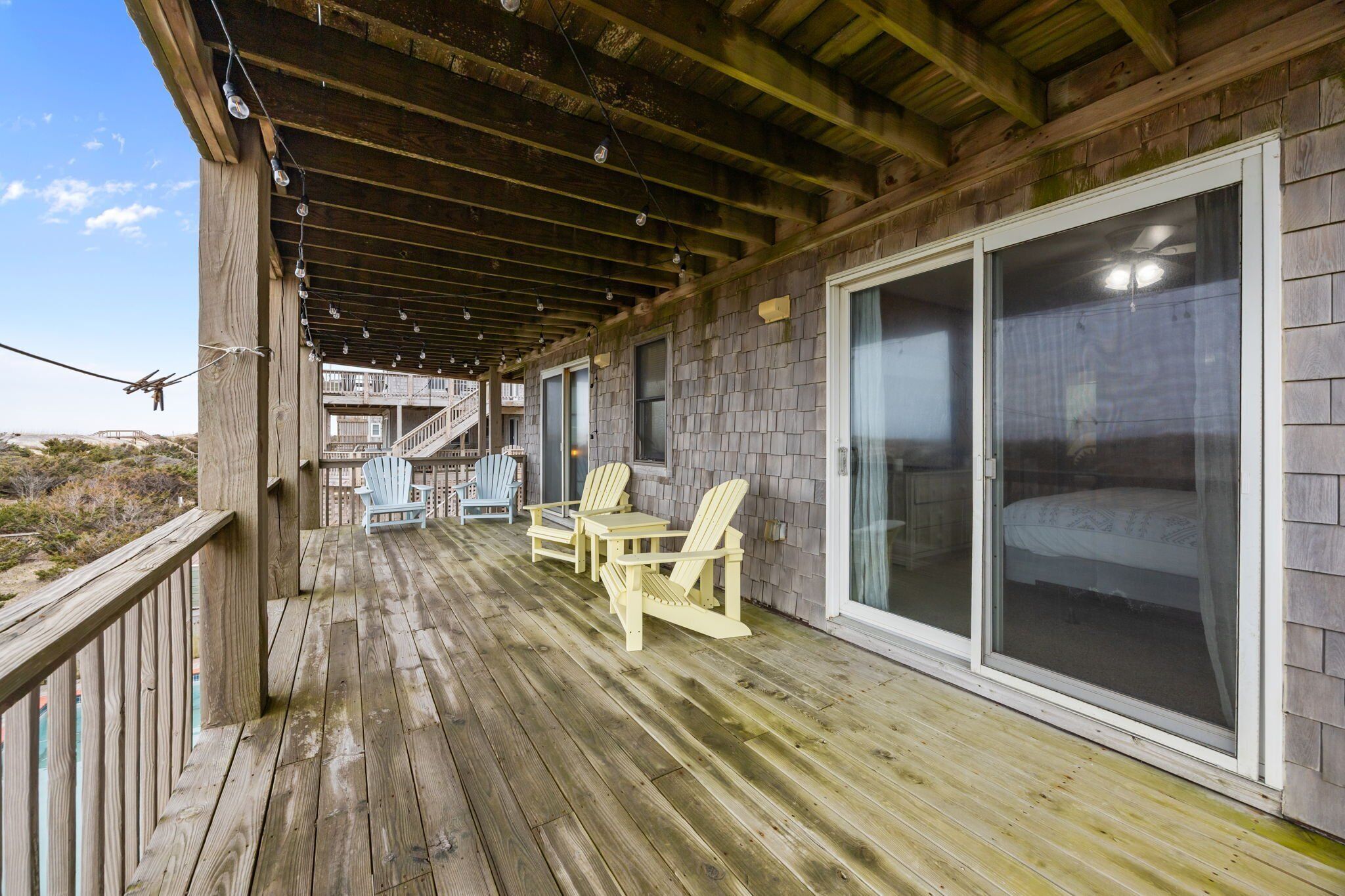 A wooden deck with Adirondack chairs and a glass door leading to a bedroom.