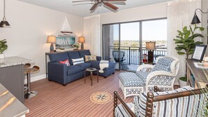 A spacious living area with a blue sofa, a small table, and a balcony with wicker chairs.