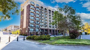 A multi-story hotel with a brick facade, large windows, and a landscaped front yard.