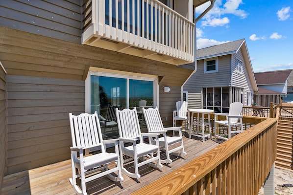 Une terrasse en bois avec des chaises Adirondack blanches et une balustrade en bois.
