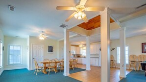 A spacious living area with a dining table and chairs, a kitchen in the background, and a ceiling fan.