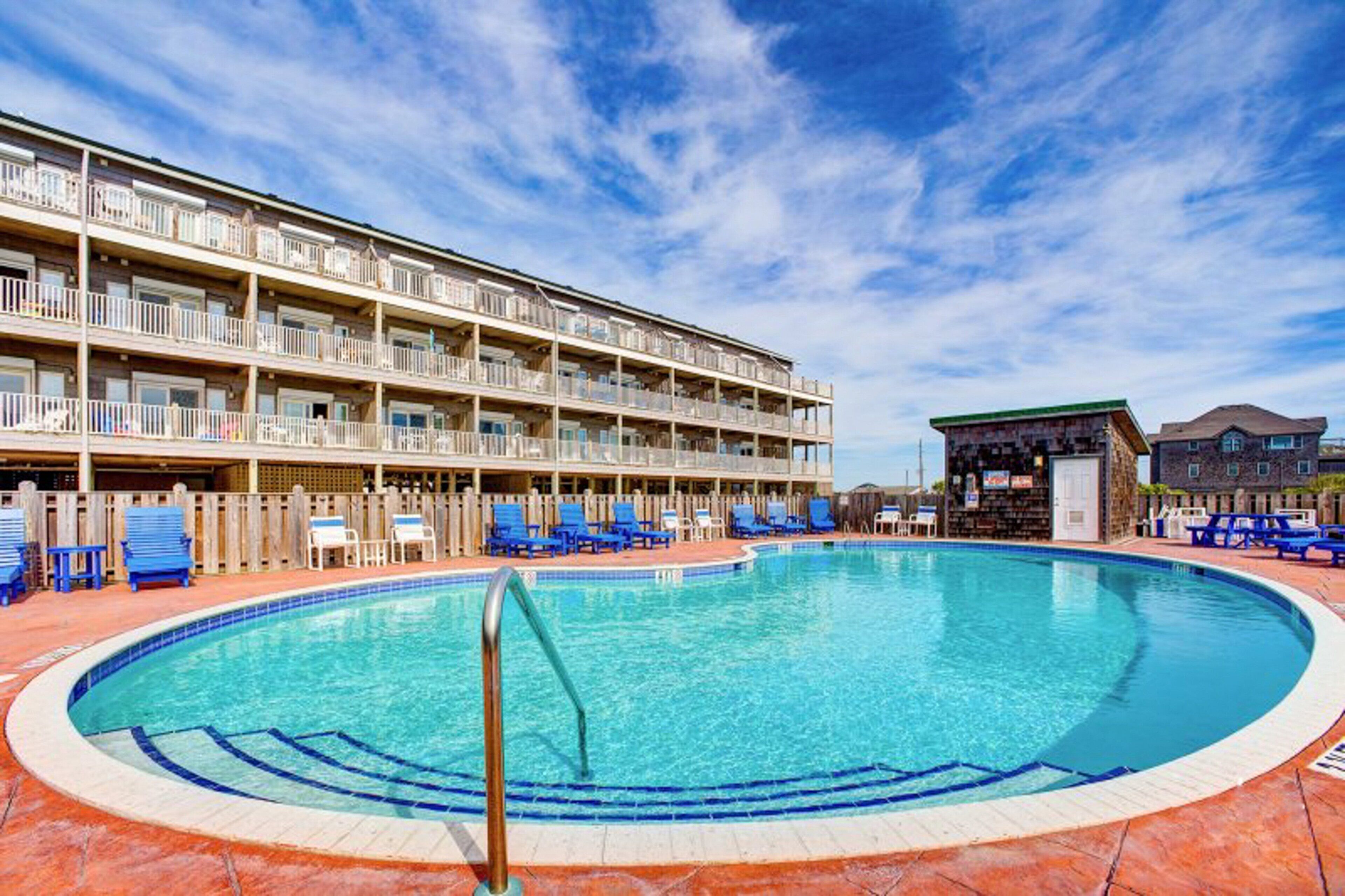 Ein Hotel mit großem Pool, mehreren Balkonen und einem hölzernen Zaun, der das Pool-Areal umgibt.