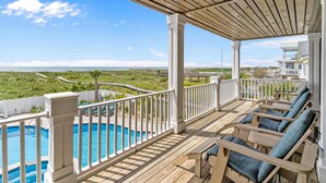 A wooden deck with a pool, lounge chairs, and a view of the ocean and greenery. - Modern Oceanfront Home with Zero-Entry Pool, Hot Tub, Outdoor Kitchen, WiFi & AC (Holden Beach)