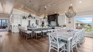 A spacious kitchen with wooden flooring, white cabinetry, and a large island with bar stools. - Modern Oceanfront Home with Zero-Entry Pool, Hot Tub, Outdoor Kitchen, WiFi & AC (Holden Beach)