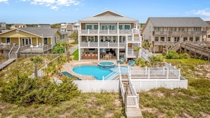 A large two-story house with a swimming pool, multiple decks, and a fenced yard. - Modern Oceanfront Home with Zero-Entry Pool, Hot Tub, Outdoor Kitchen, WiFi & AC (Holden Beach)