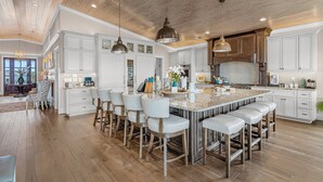 A spacious kitchen with a large island, white cabinetry, and modern pendant lighting. - Modern Oceanfront Home with Zero-Entry Pool, Hot Tub, Outdoor Kitchen, WiFi & AC (Holden Beach)