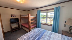 Habitación con literas, un televisor sobre una mesita pequeña, una ventana con cortinas y una lámpara en una mesita de noche.