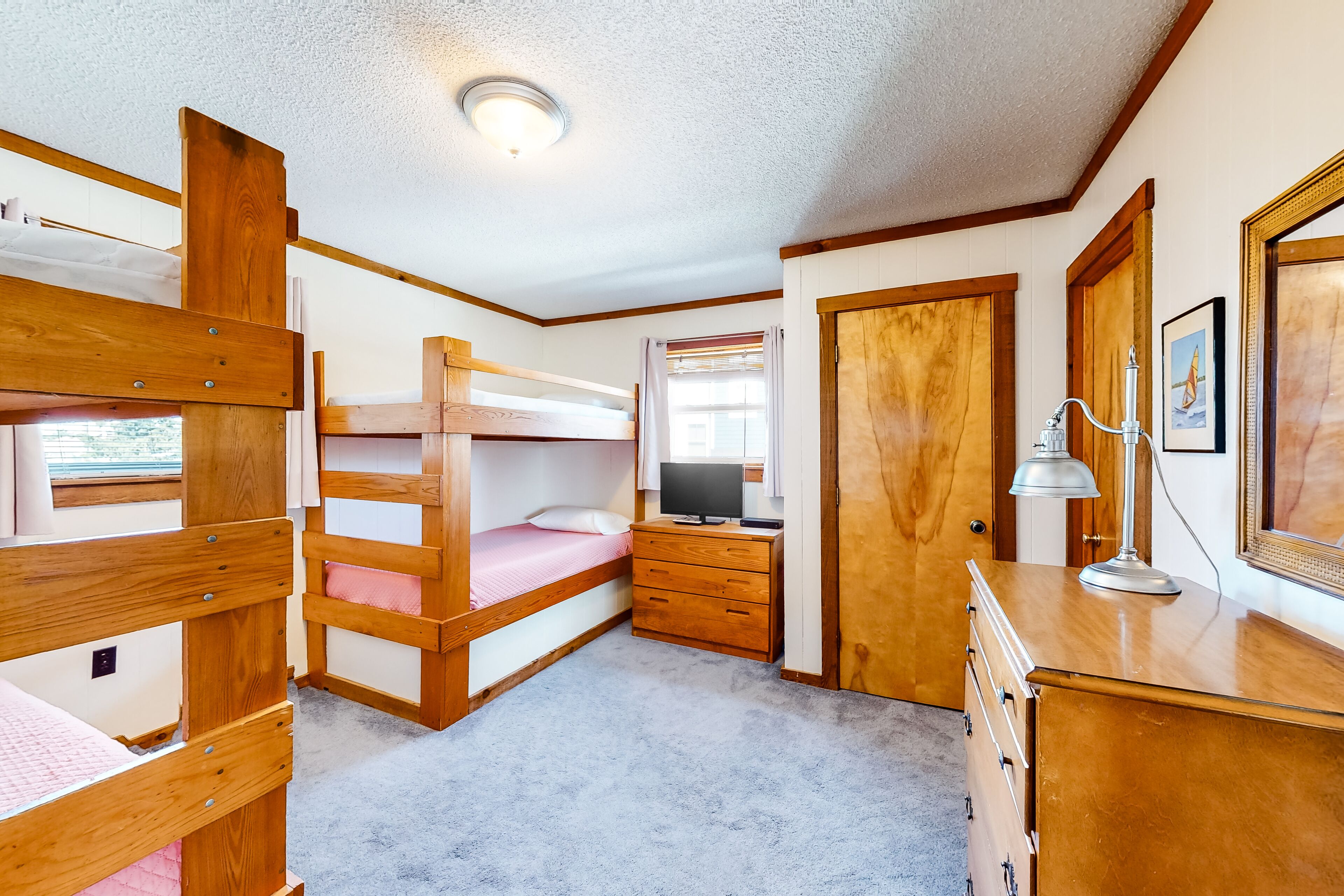 A bunk bed room with a wooden dresser, a desk with a lamp, and a television.