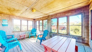A covered patio with wooden flooring, a picnic table, and blue and pink chairs. - Forever June 383: Near the beach w/deck! (Avon)