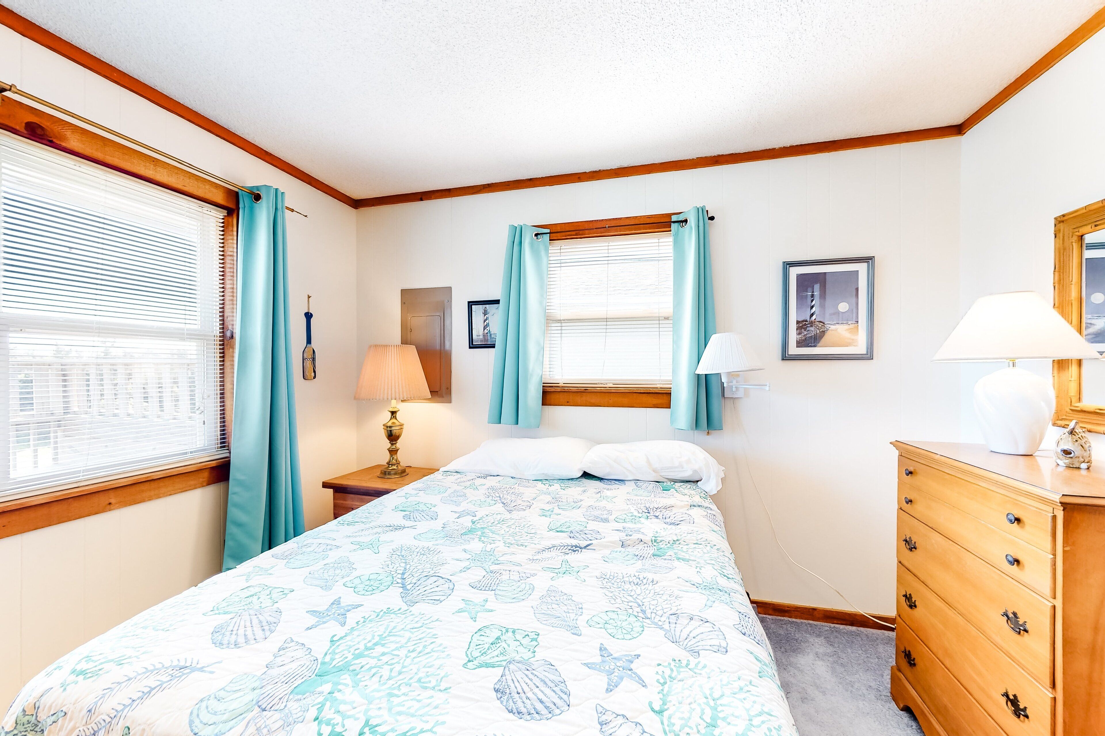 A bedroom with a bed, a dresser, a nightstand, a lamp, and a window with curtains.