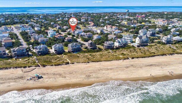 An aerial view of a coastal residential area with houses, a beach, and a water tower. - Forever June 383: Near the beach w/deck! (Avon)