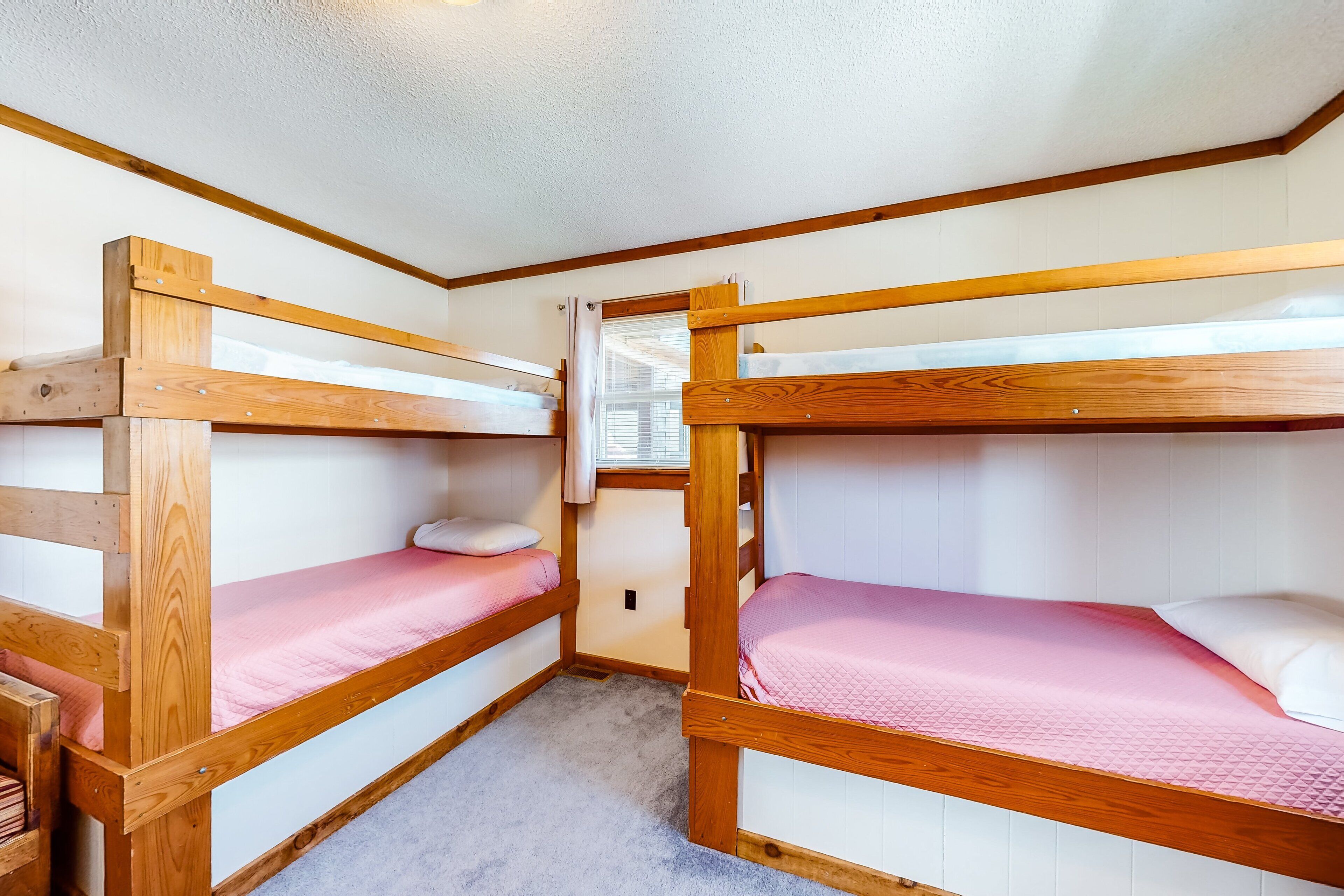 A bunk bed room with wooden frames and pink bedding.