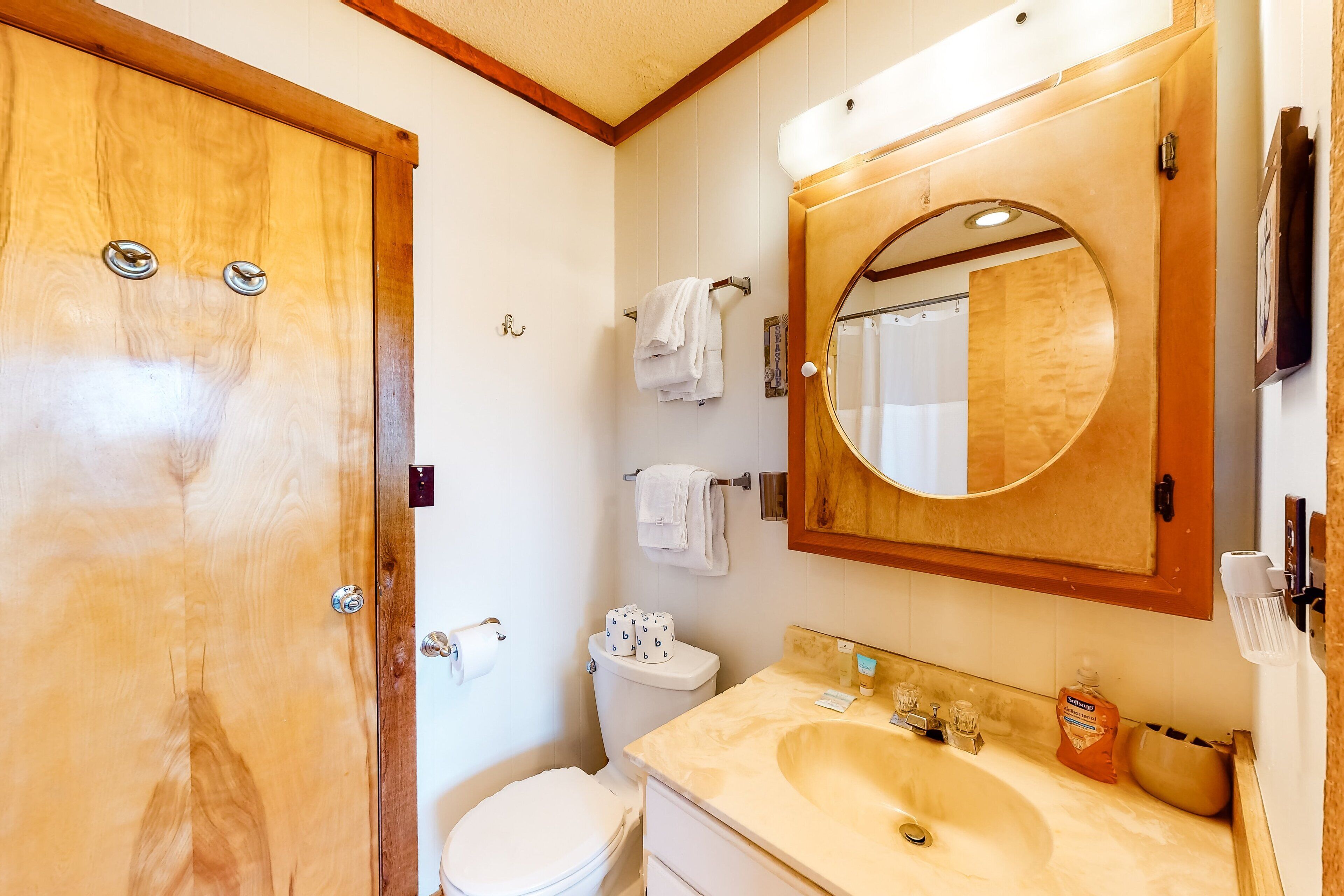 A bathroom with a wooden door, a toilet with a white lid, a sink with a mirror above it, and a towel rack with towels.