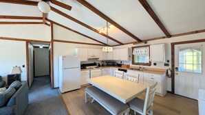 A compact kitchen with a central island, white cabinetry, and a dining area with a bench. - Forever June 383: Near the beach w/deck! (Avon)