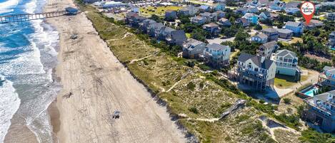 An aerial view of a coastal residential area with houses, a beach, and a pier.