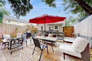 Un patio al aire libre con una mesa, sillas, un paraguas rojo y una terraza de madera.