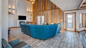 Een ruime zithoek met een grote blauwe modulaire bank, houten wanden en een flatscreen televisie aan de muur.