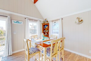 Un coin repas avec une table et des chaises en bois, une étagère décorative où sont exposés divers objets, et une vue sur l’extérieur.