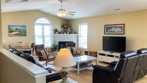 Un salon comprenant un canapé, des fauteuils, un téléviseur, une cheminée et un ventilateur de plafond.
