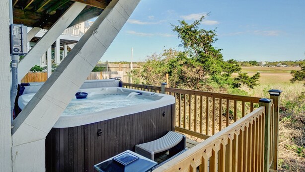 Un bain à remous sur une terrasse en bois, avec vue sur un champ et des arbres.