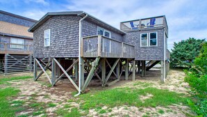 Une construction en bois à deux étages, dotée d’une terrasse et d’un balcon, soutenue par des piliers en métal.