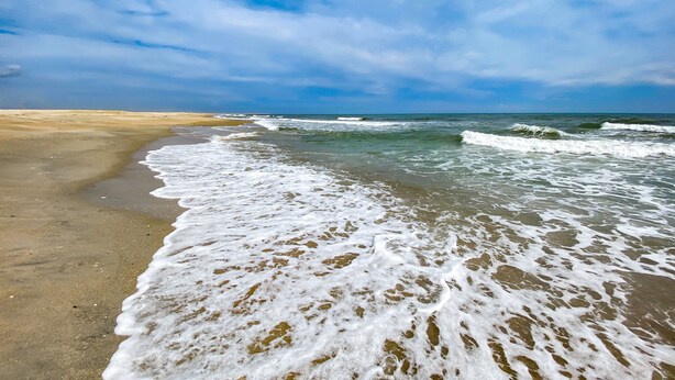 Une plage où les vagues viennent lécher le rivage sous un ciel partiellement nuageux.
