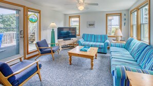Un salon avec un téléviseur, un canapé à rayures bleues, des chaises en bois et un ventilateur de plafond.