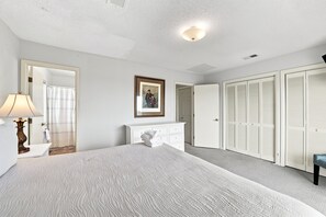 Une chambre à coucher avec un grand lit, une commode, un miroir, un tableau encadré et un ensemble d’armoires blanches.