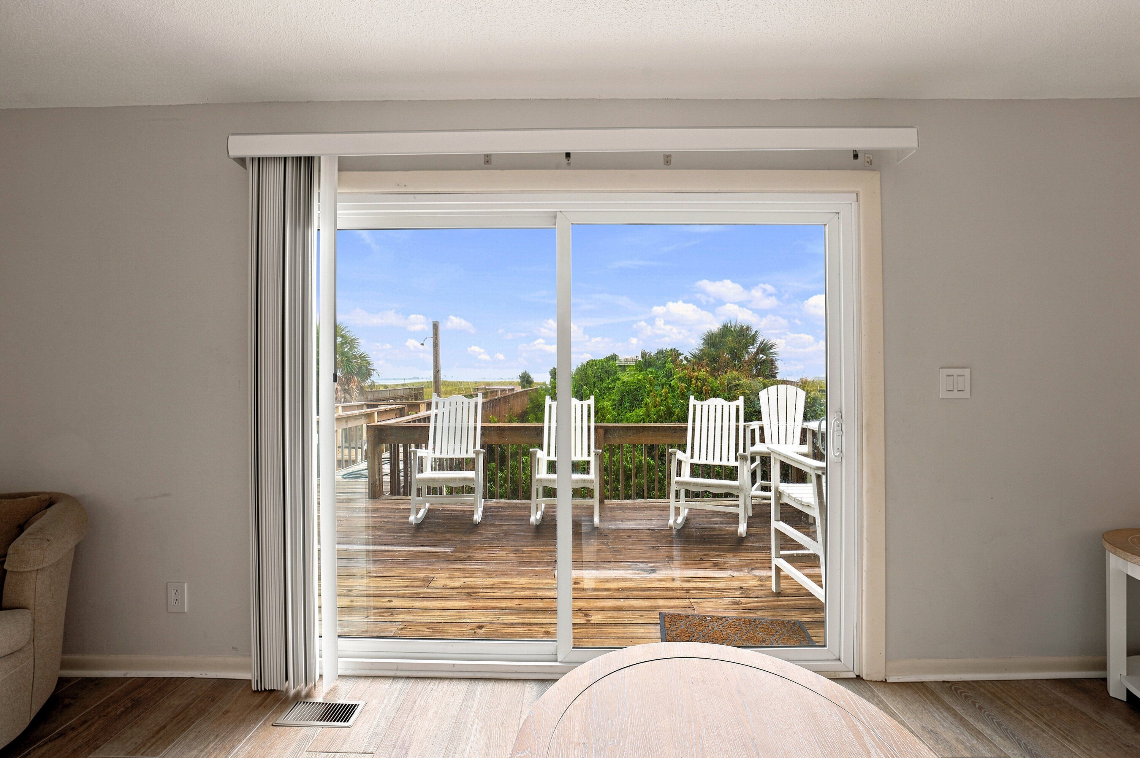 A room with a sliding glass door leading to an outdoor deck with white chairs.