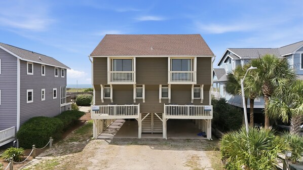 A two-story building with a balcony, a covered entrance, and a view of the ocean. - Oceanfront home with WiFi, central AC, washer/dryer - dogs welcome (Holden Beach)